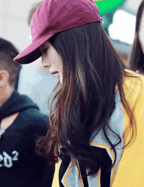 杨幂现身机场打扮时尚，黄色上衣搭配牛仔短裙，低头耳语笑容温暖