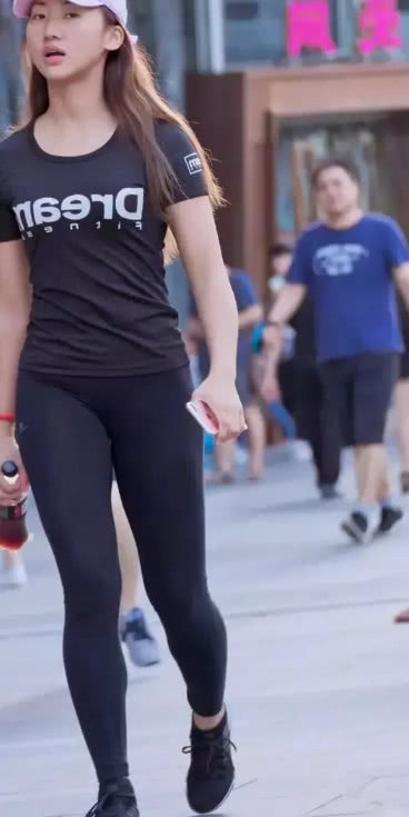 逛街的小姐姐一身黑色紧身运动衣展现好身材，可手里的瓶子却出卖