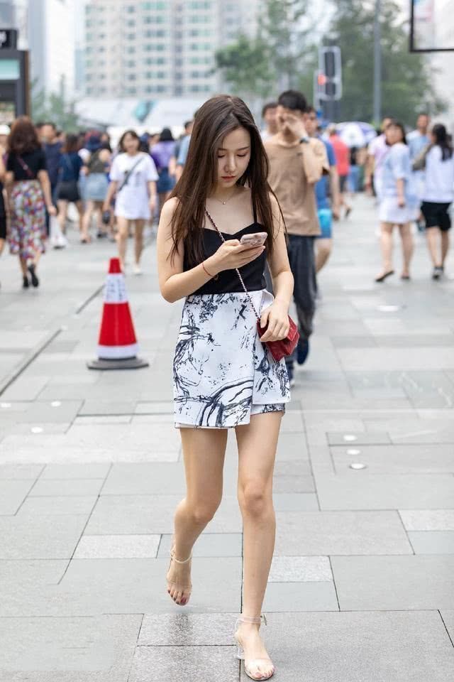 美女|街拍:低头看手机的美女,简洁的吊带背心搭配半身裙,简洁大方又不失美感