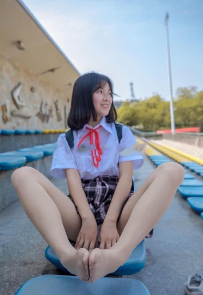 穿着校服的小姐姐坐在球场看台上，露出肉色丝袜包裹的小脚丫