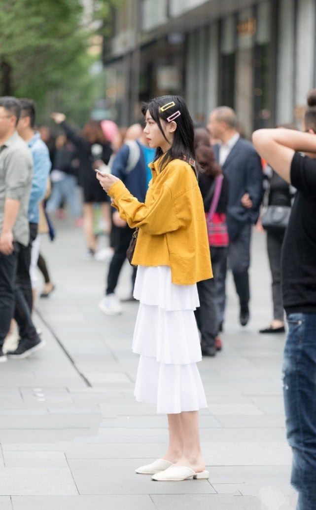 美女|街拍:低头看手机的美女,简洁的吊带背心搭配半身裙,简洁大方又不失美感