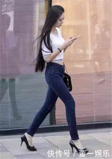 低头玩手机小姐姐身穿蓝色紧身牛仔裤搭配白色漏脐装，走起路来臀