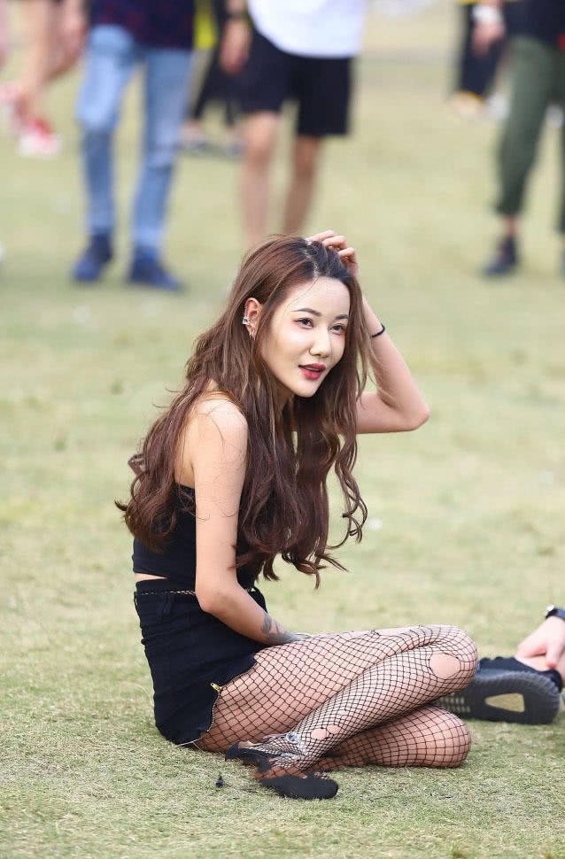 穿着紧身抹胸的小姐姐坐在草地上，轻拂头发时的眼神很有女人味