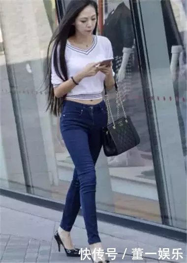 低头玩手机小姐姐身穿蓝色紧身牛仔裤搭配白色漏脐装，走起路来臀