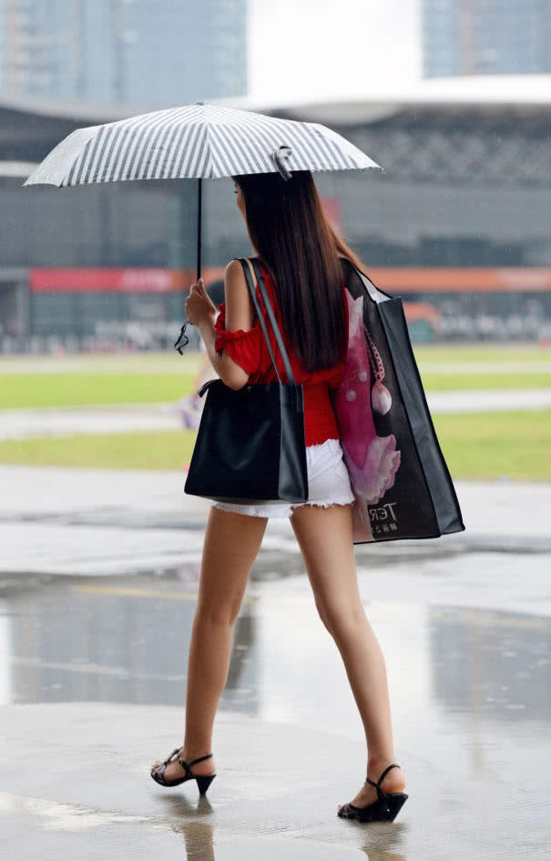 时尚小姐姐雨天上街，小热裤勾勒出修长美腿，伞下的她显得更加诱