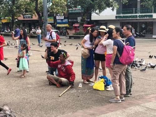 中国游客来泰国清迈旅游，在广场上拍照，竟专门找当地人来吓鸽子