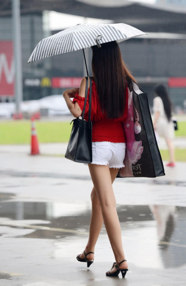 时尚小姐姐雨天上街，小热裤勾勒出修长美腿，伞下的她显得更加诱