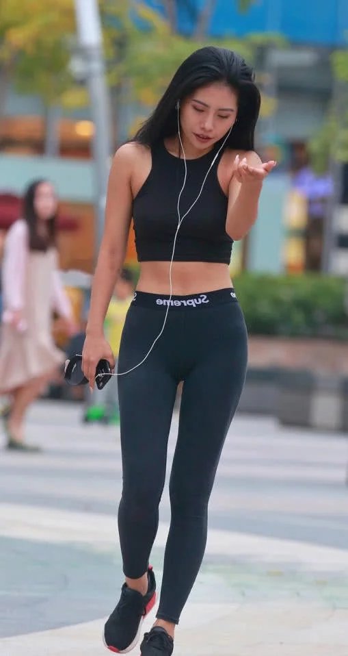 时尚小姐姐穿着紧身裤搭配抹胸装，在广场上玩街拍，搞怪的姿势很