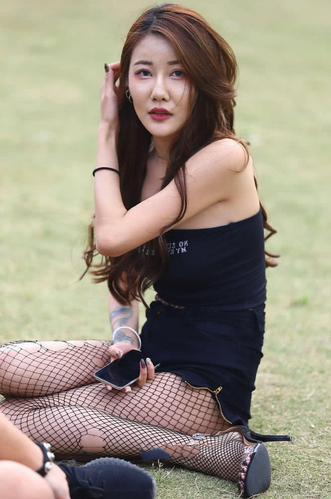 穿着紧身抹胸的小姐姐坐在草地上，轻拂头发时的眼神很有女人味
