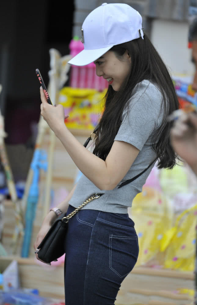 甜美小姐姐牛仔裤勾勒丰满弧线，低头拍照成了一道时尚风景线