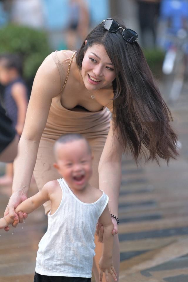 时尚辣妈，身穿肉色吊带连衣裙，俯身牵着孩子的手画面感好美！
